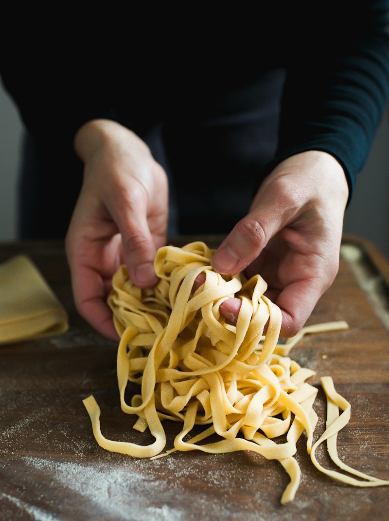 Homemade pasta fettuccini in my hands, suspended over a wooden surface.