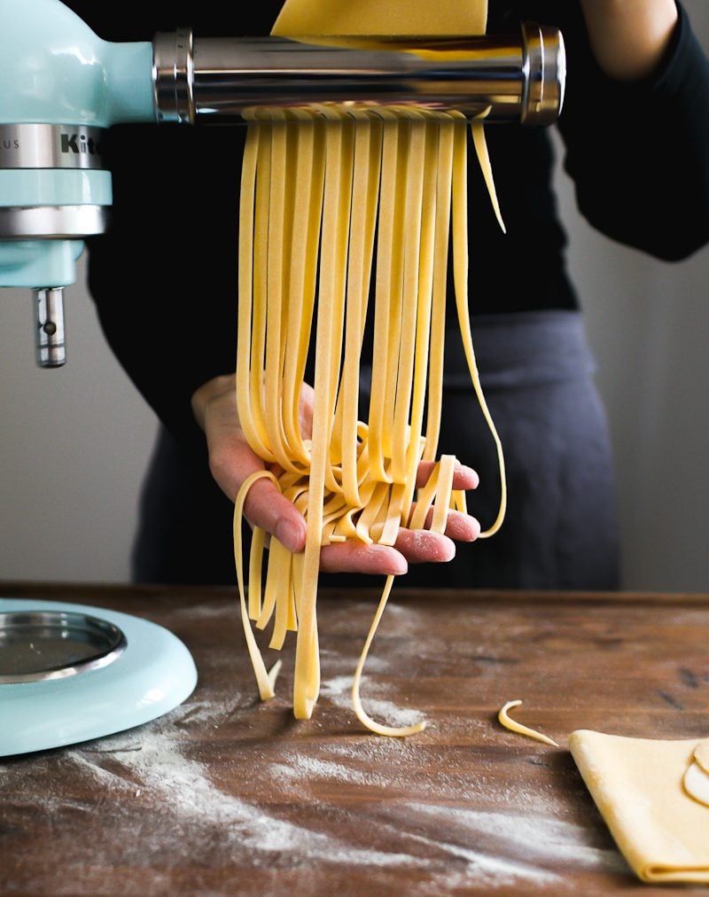 Fresh homemade pasta (e.g. long fettuccini strands), coming through a Kitchen Aid stand mixer pasta attachment.