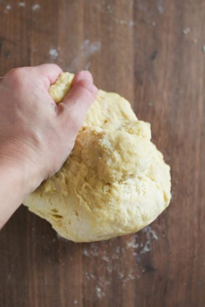 Homemade pasta dough kneading on a dark wooden surface.