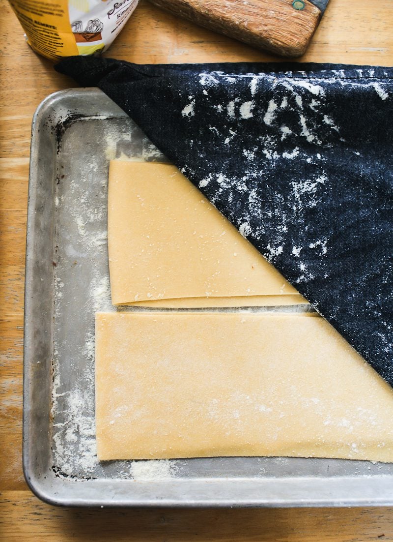 Fresh pasta sheets folded in half on a flour dusted sheet pan.