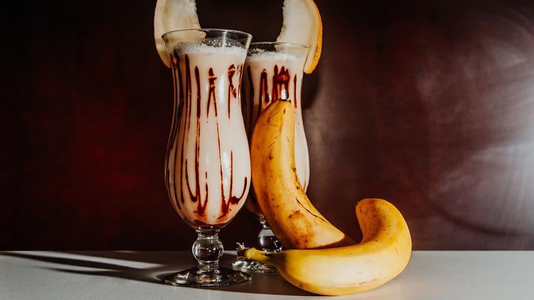 Two banana colada cocktails in glasses next to two bananas