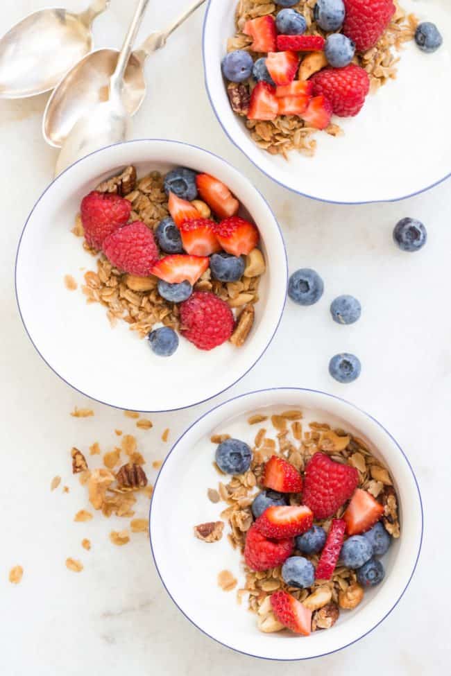 Best Granola Recipe Three white bowls filled with yogurt, healthy granola and mixed berries.